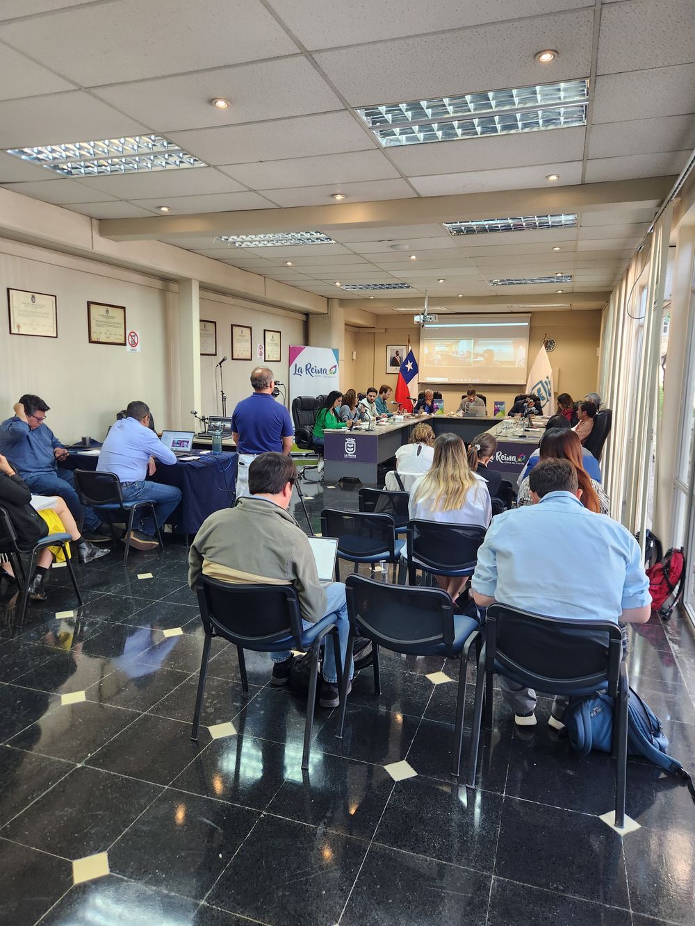 Municipal council room with councilors around a U-shaped table and visitors in the foreground