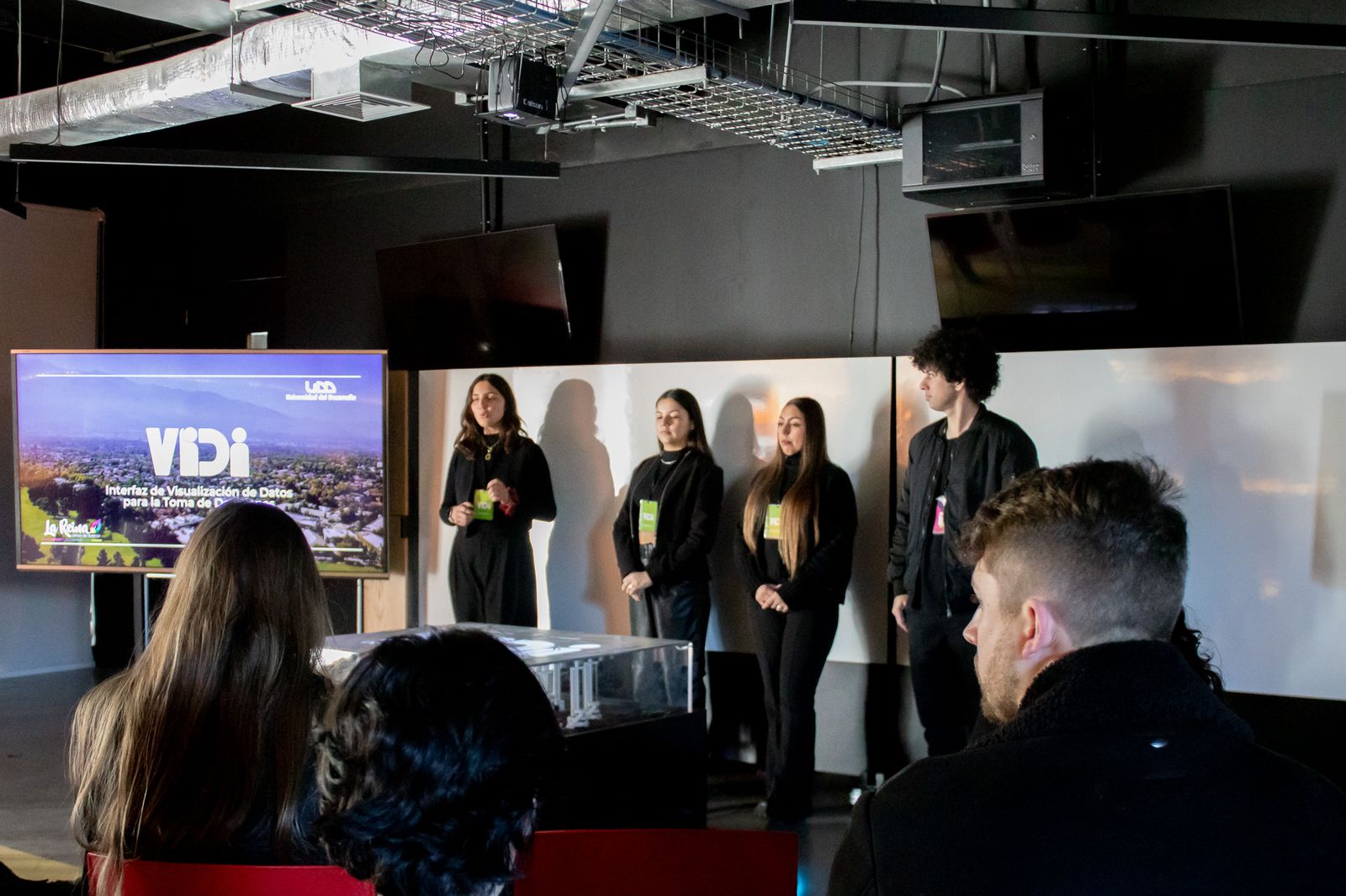 Four members of the group presenting in front of the screen and the table, with the audience in the foreground