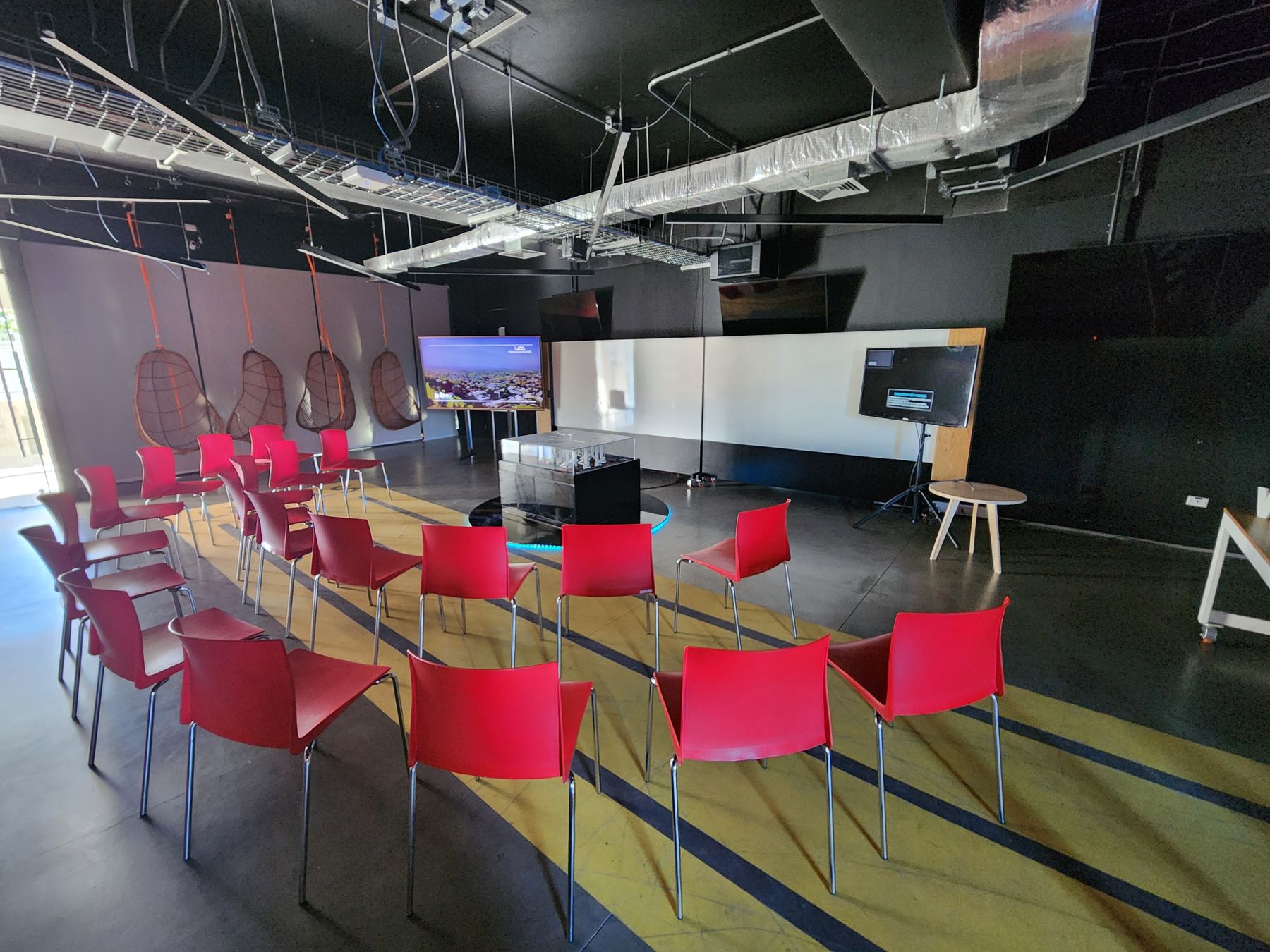 The room before the final presentation: a semicircle of red chairs facing the table, with a screen on each side